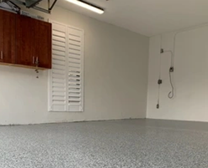 A garage with white window, red wooden mounted cabinet, and an epoxy floor.